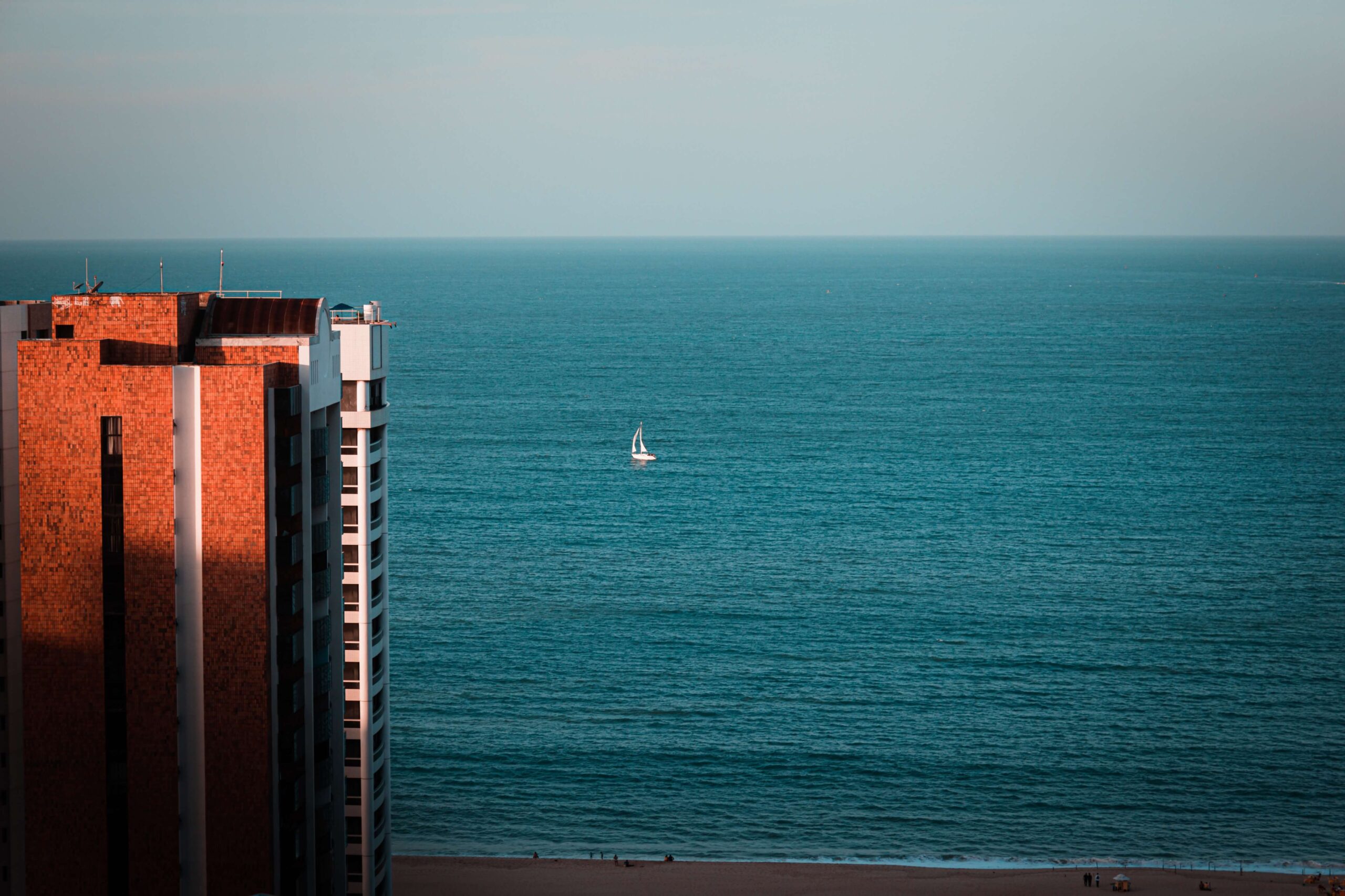 Prédio em frente ao mar de Fortaleza com um barco branco navegando